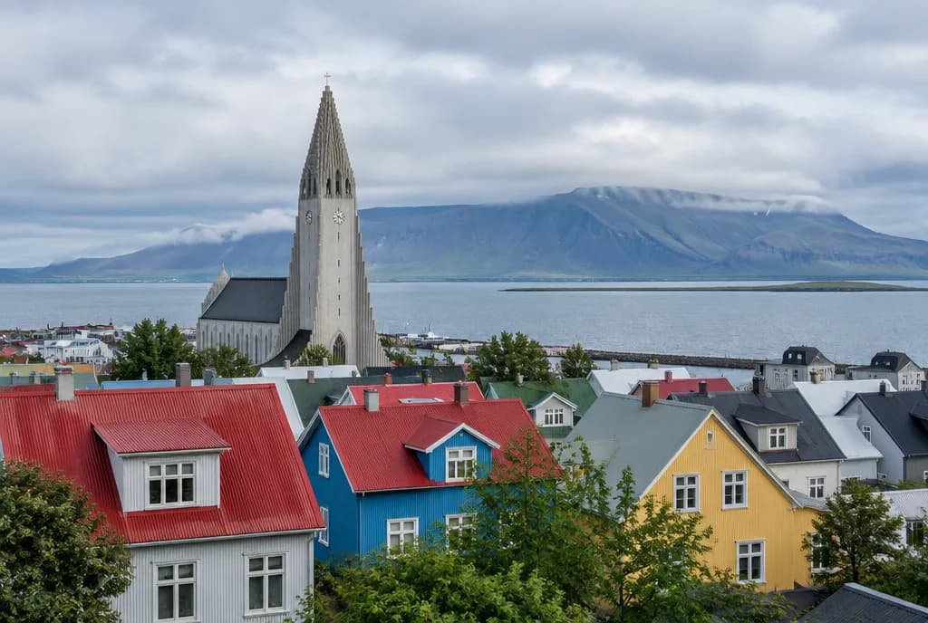 Hallgrímskirkja over Reykjavíks røde og fargerike hustak, med bukten og et flatt fjell bak
